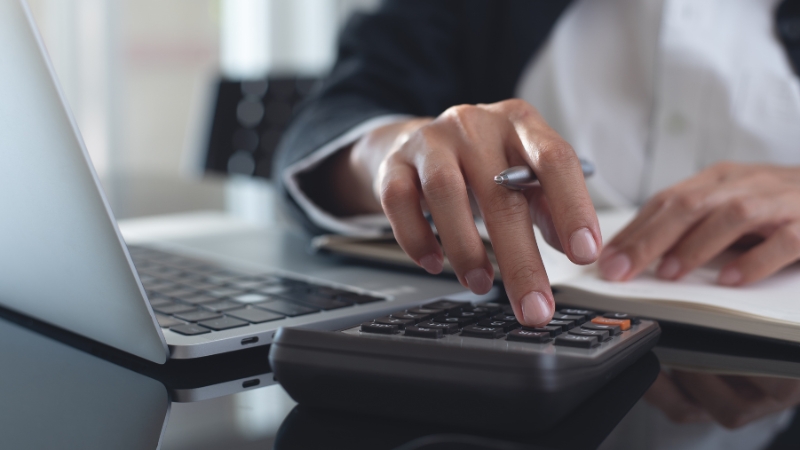 Knjigovođa računa troškove na digitronu pored laptopa dok radi administrativne i finansijske poslove