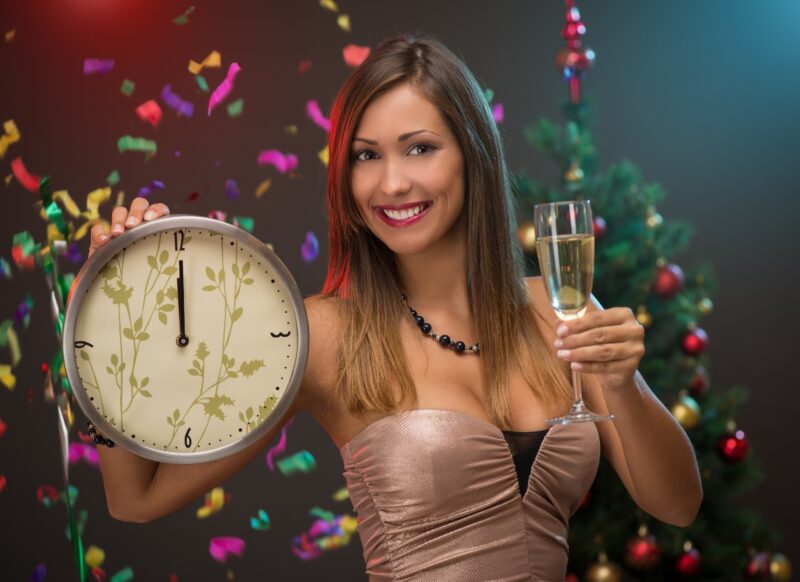devojka drži sat u jednoj ruci a u drugoj šampanjac, iza nje lete konfete 