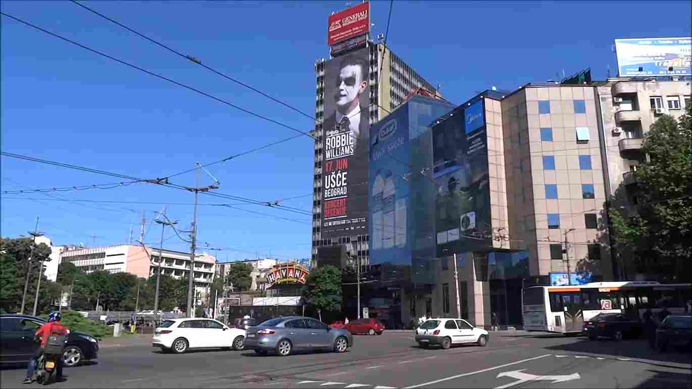 Prometna raskrsnica na Slaviji sa velikim reklamama na fasadama zgrada.