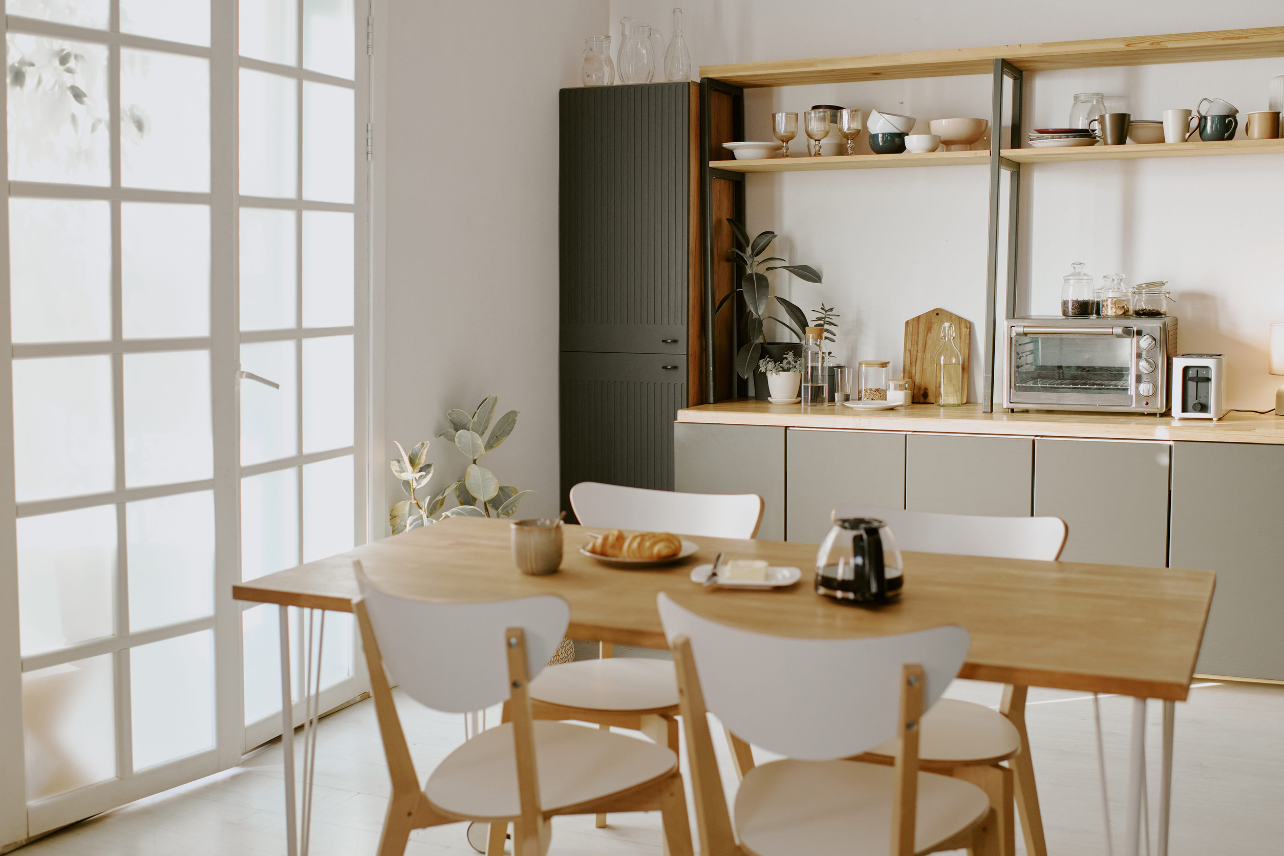 Svetla kuhinja sa otvorenim policama, visokim elementima i trpezarijskim stolom kao primer funkcionalnog uređenja manjeg prostora